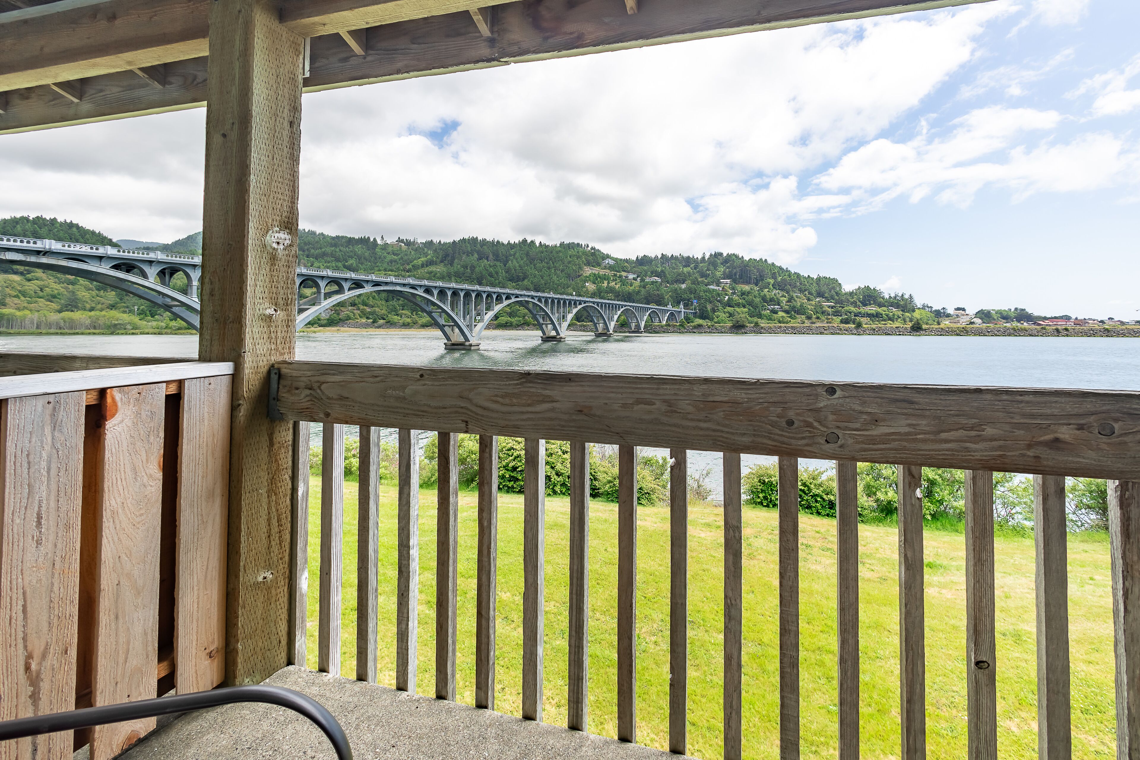 A wooden deck with a view of a bridge over a river, surrounded by greenery.