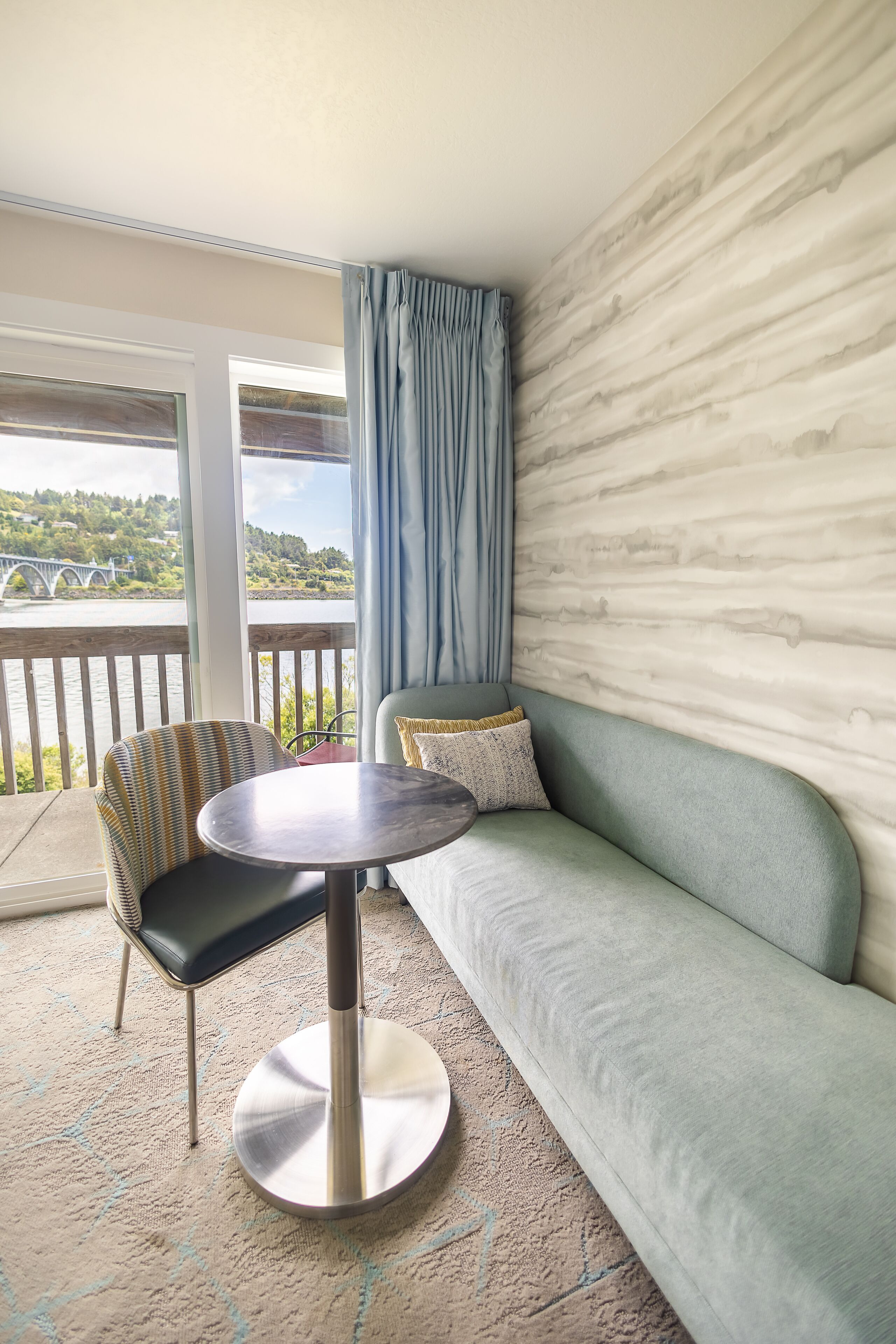 A room with a sofa, a chair, a round table, and a view of a bridge and river.