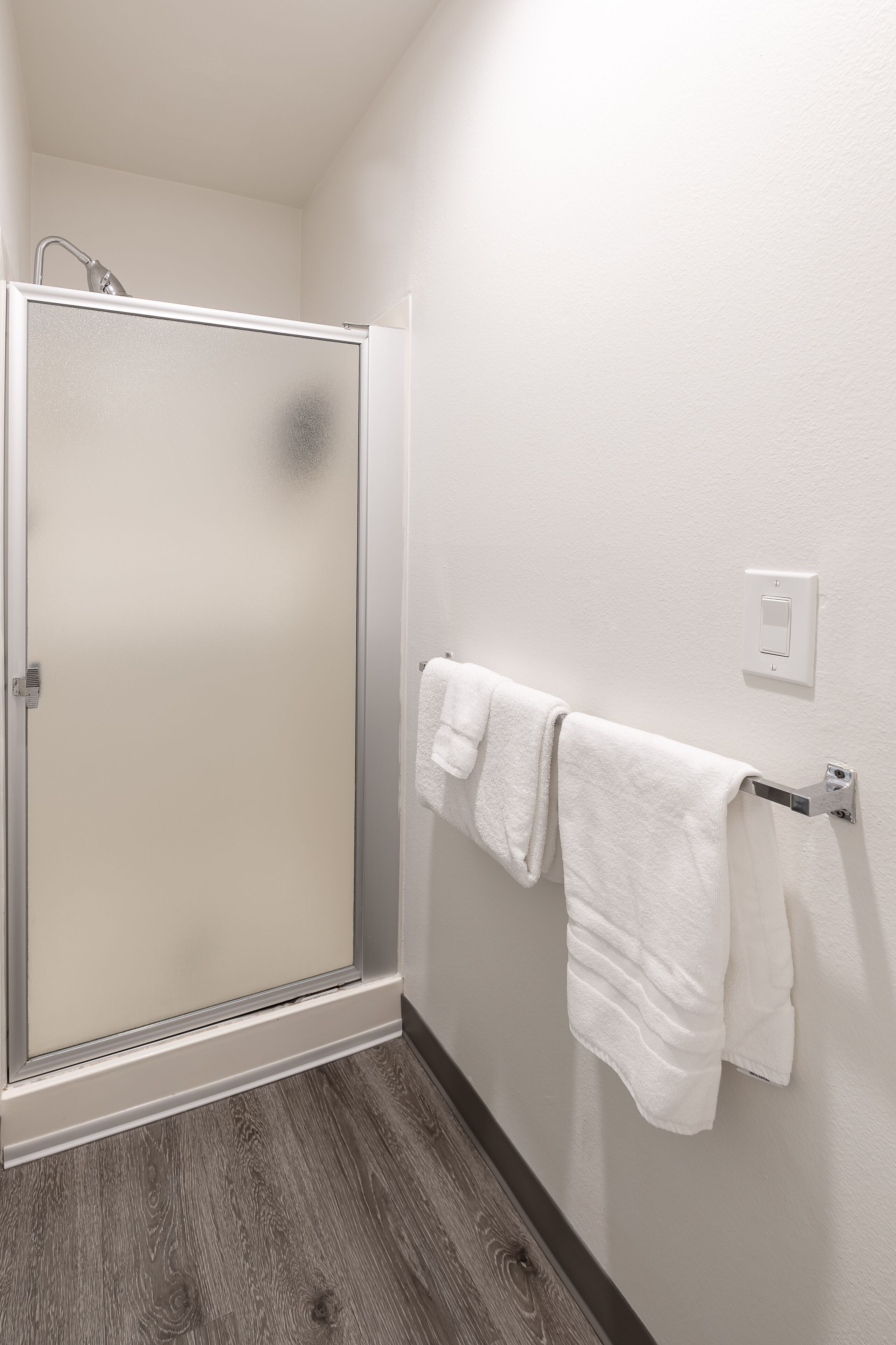 A bathroom with a glass shower door, a towel rack with two towels, and a light switch on the wall.
