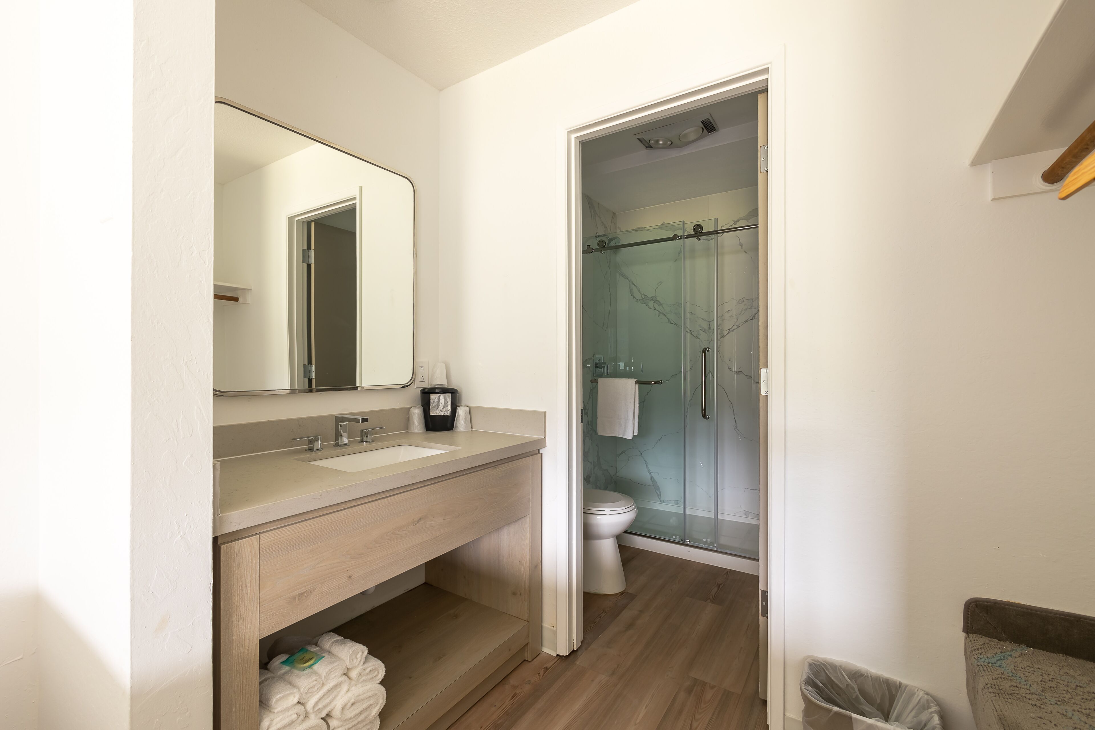 A bathroom with a wooden vanity, a large mirror, a glass shower enclosure, and a toilet.
