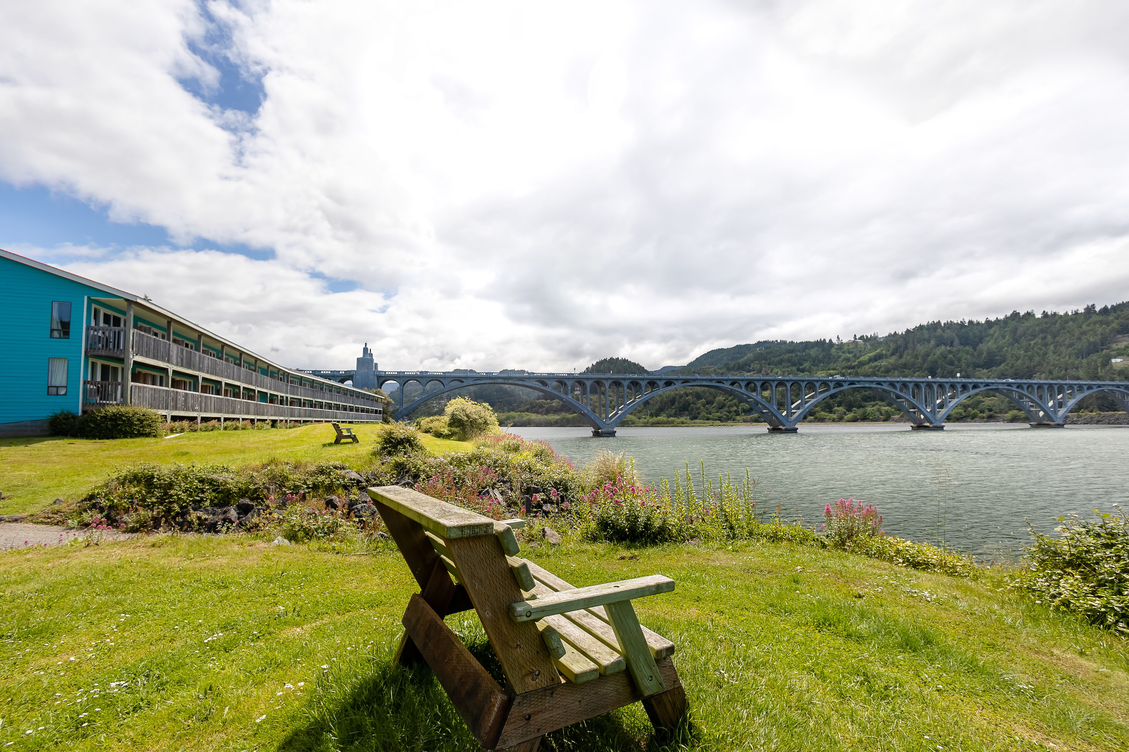 A lakeside view with a wooden bench, a bridge, and a building with a blue facade.