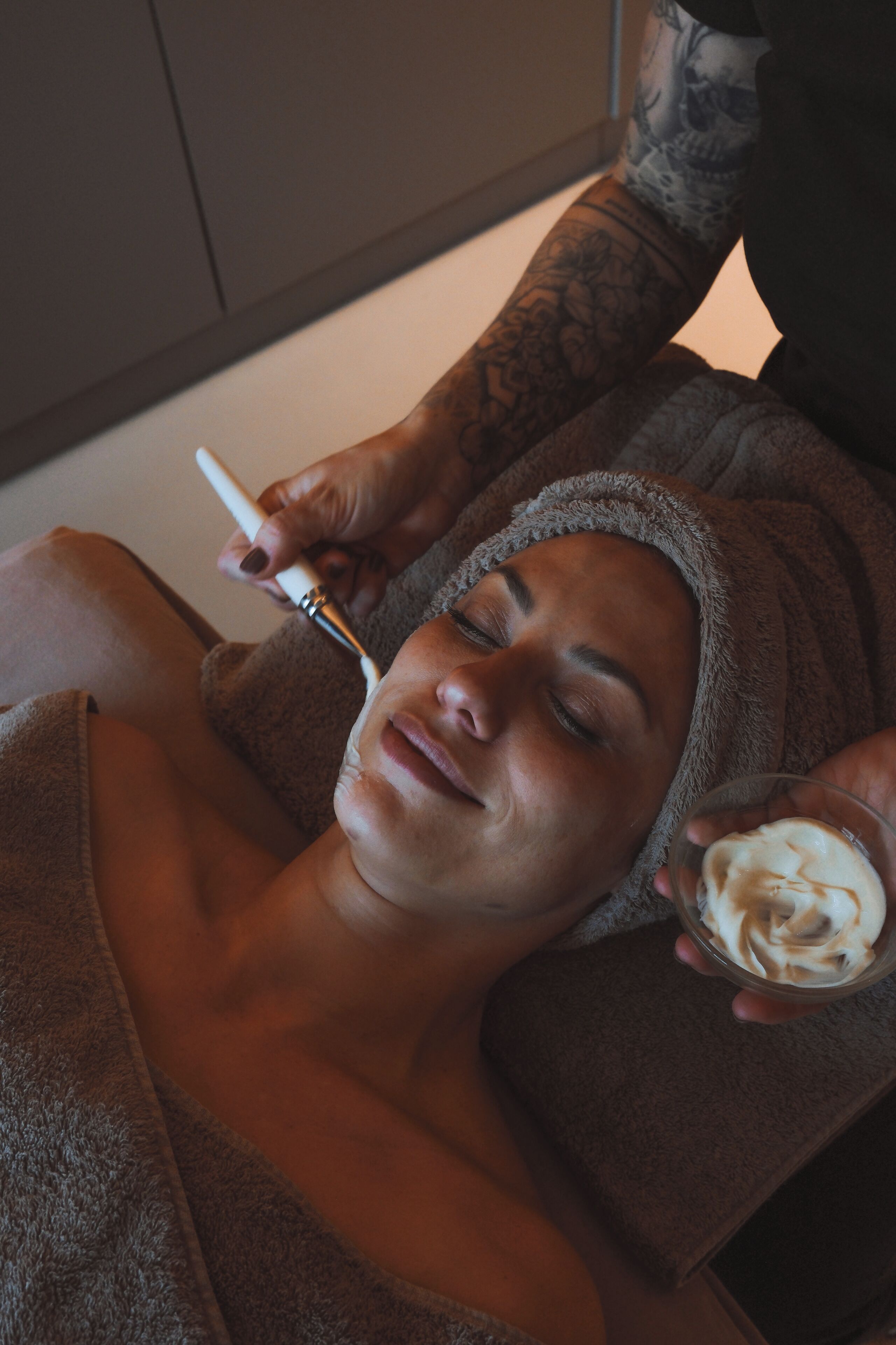 Una persona recibiendo un tratamiento facial en una habitación, con una toalla alrededor de la cabeza.