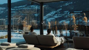 Un área de spa con dos sillones reclinables, una mesita y vistas a montañas nevadas a través de amplios ventanales.