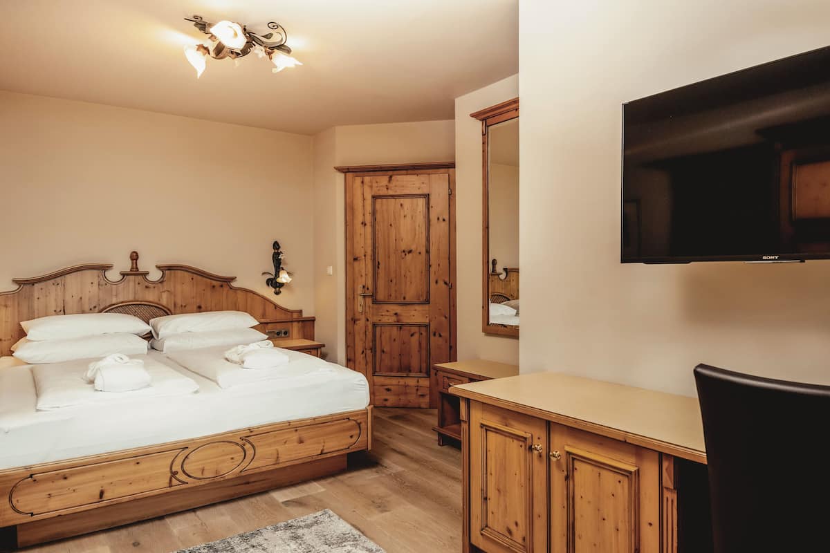 A bedroom with a wooden bed, a television mounted on the wall, and a wooden wardrobe.