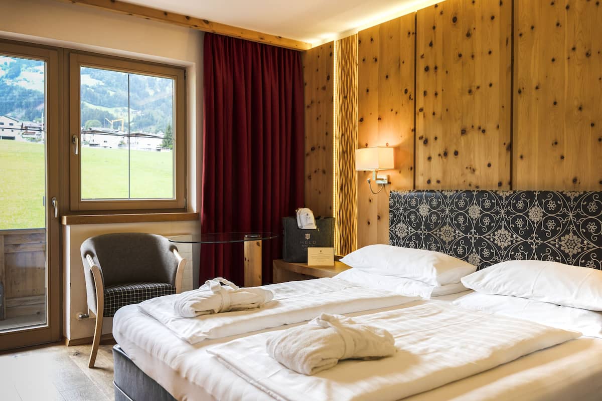 A hotel room with a bed, a chair, a desk with a lamp, and a view of the outdoors.