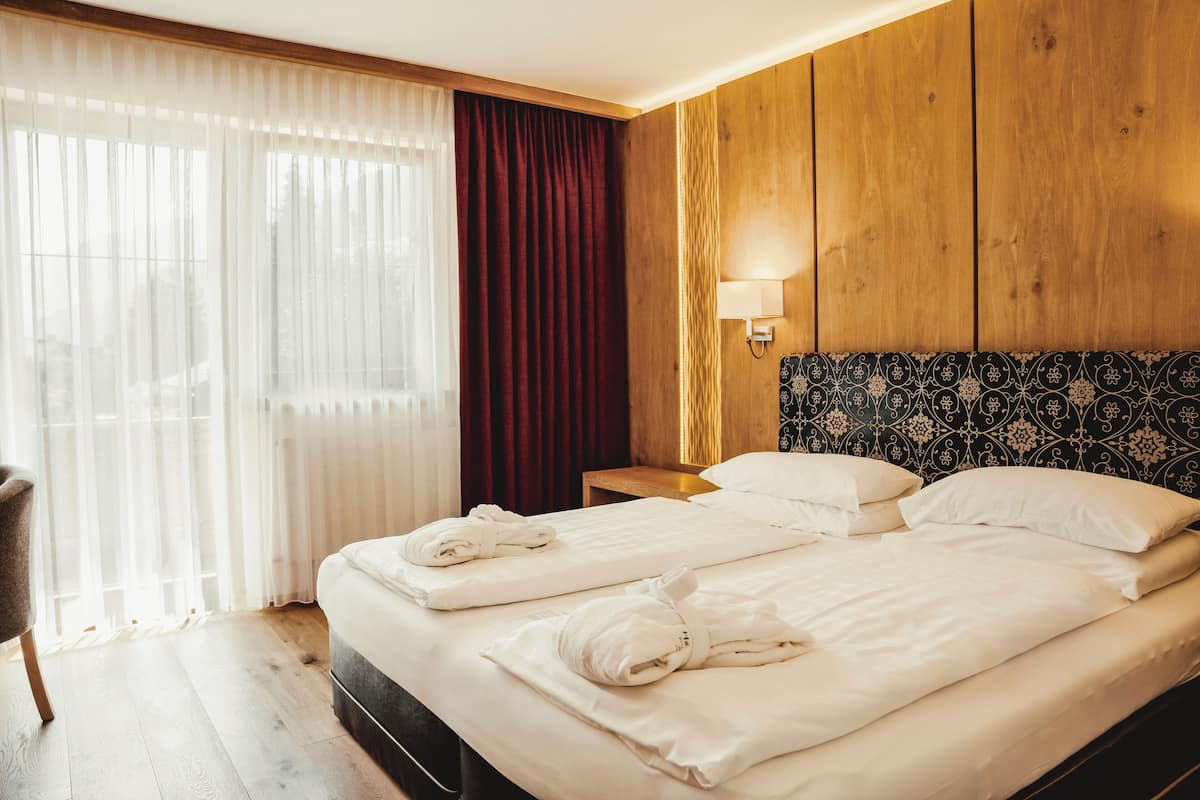 A hotel room with a wooden headboard, a bed with white linens, a bedside table with a lamp, and a chair.