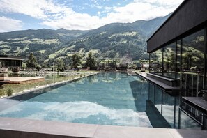 Una piscina con vistas a la montaña, un edificio moderno con grandes ventanales y una zona de terraza.