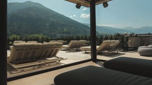 A modern outdoor seating area with lounge chairs and a sofa, overlooking a mountainous landscape. - HELD - Hotel & SPA (Fuegen)