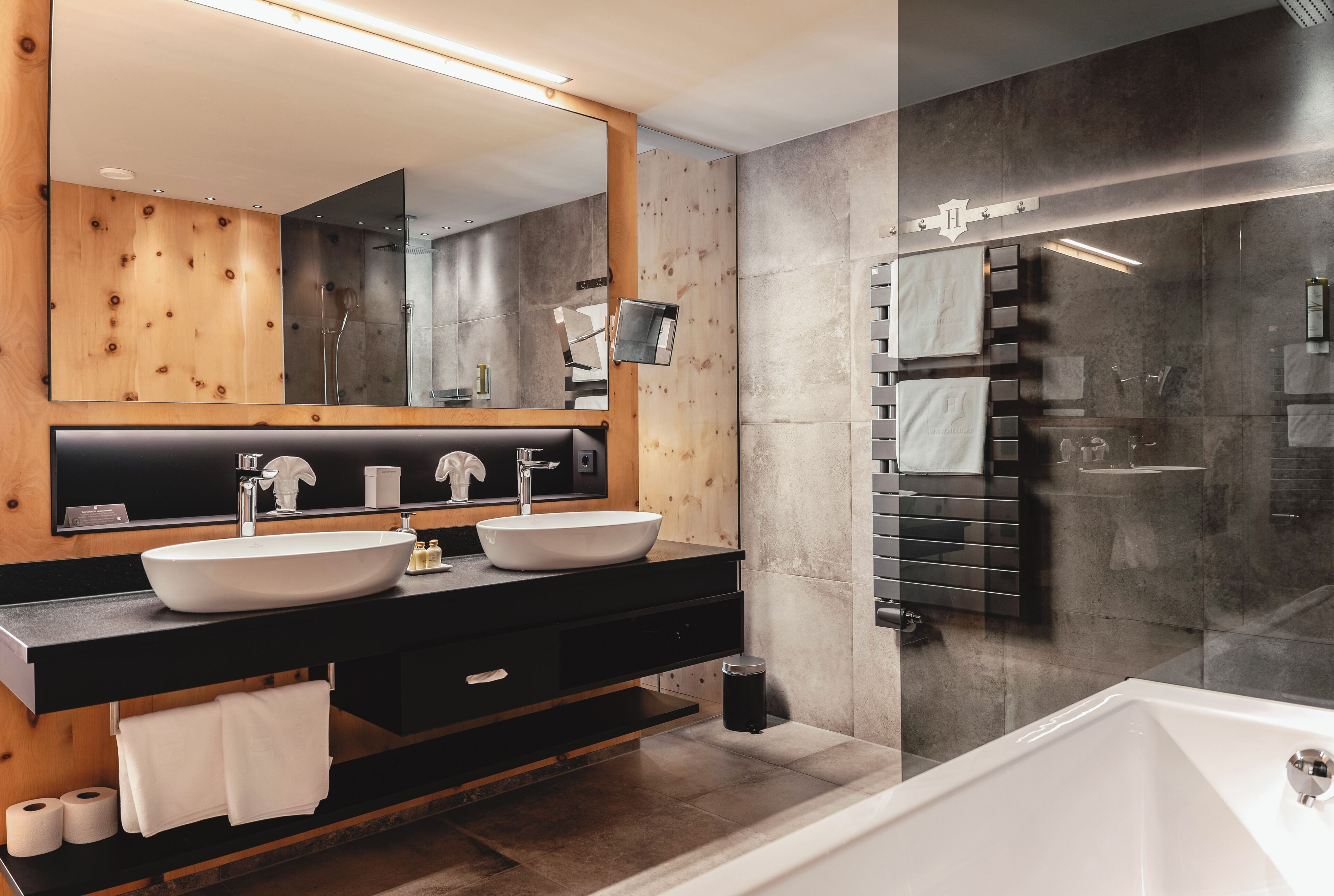 A modern bathroom with a large mirror, two sinks, a bathtub, and a glass-enclosed shower.