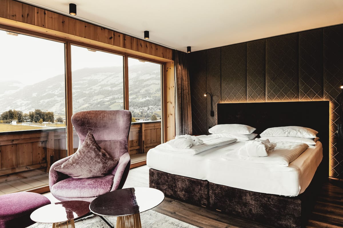 A bedroom with a large window, a bed, a chair, and a small table.