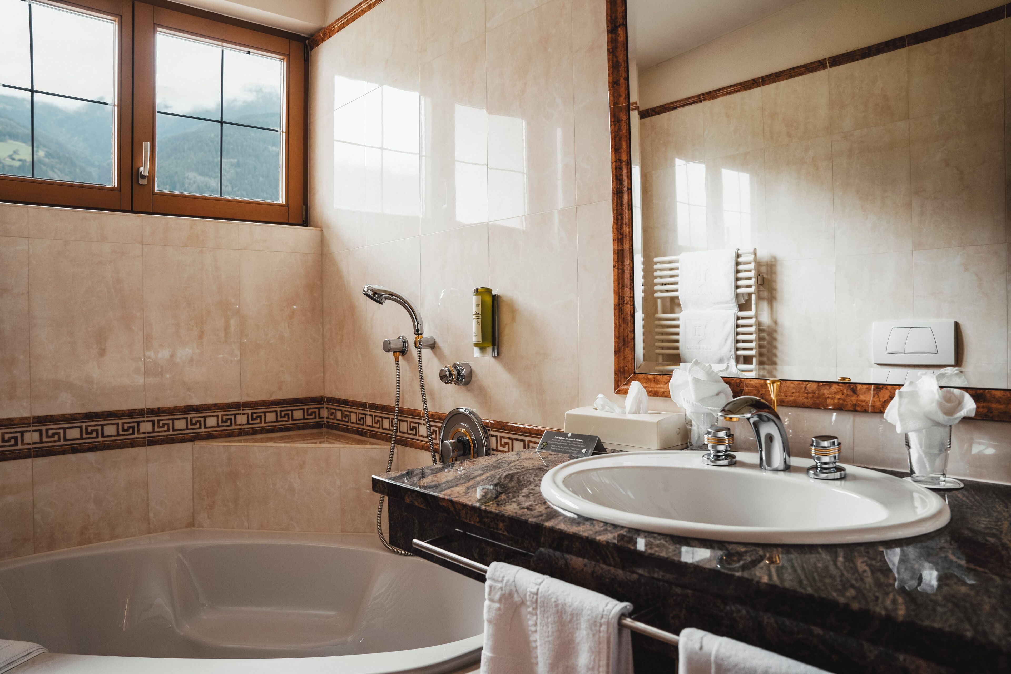 A modern bathroom with a bathtub, two sinks, a large mirror, and a window with a view of mountains.