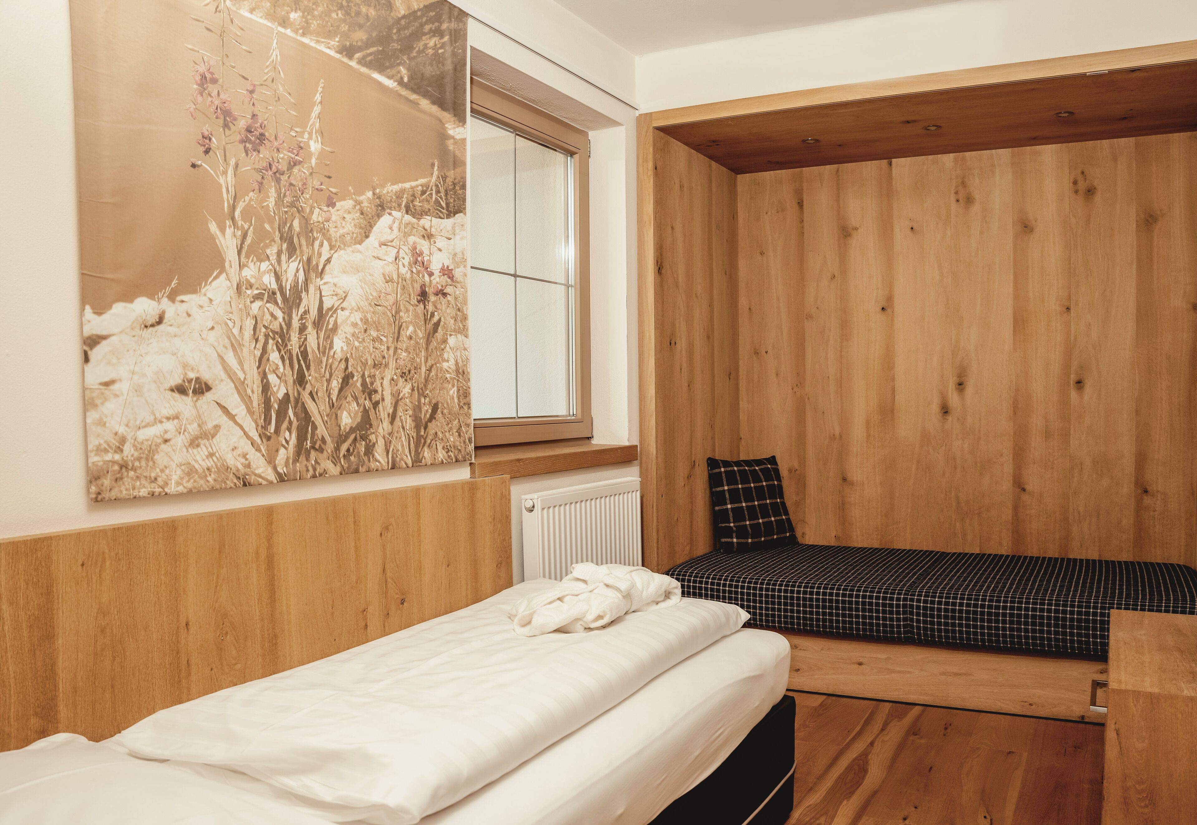 A bedroom with a wooden headboard, a bed with white linens, a black and white checkered mattress, and a large window with a view of a snowy landscape.