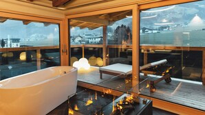 Un baño moderno con una bañera grande, una chimenea con cerramiento de vidrio y vistas a un paisaje nevado.