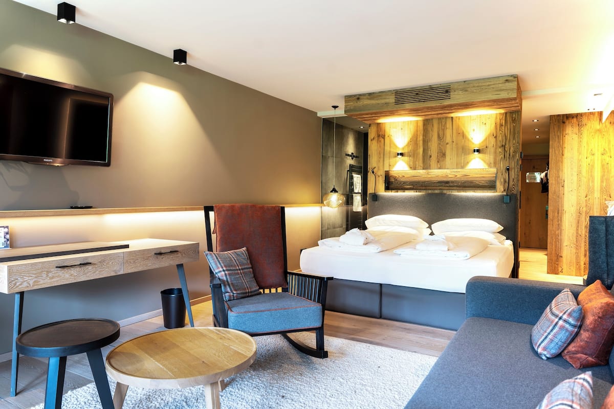 A modern bedroom with a bed, a desk, a chair, a sofa, and a television.
