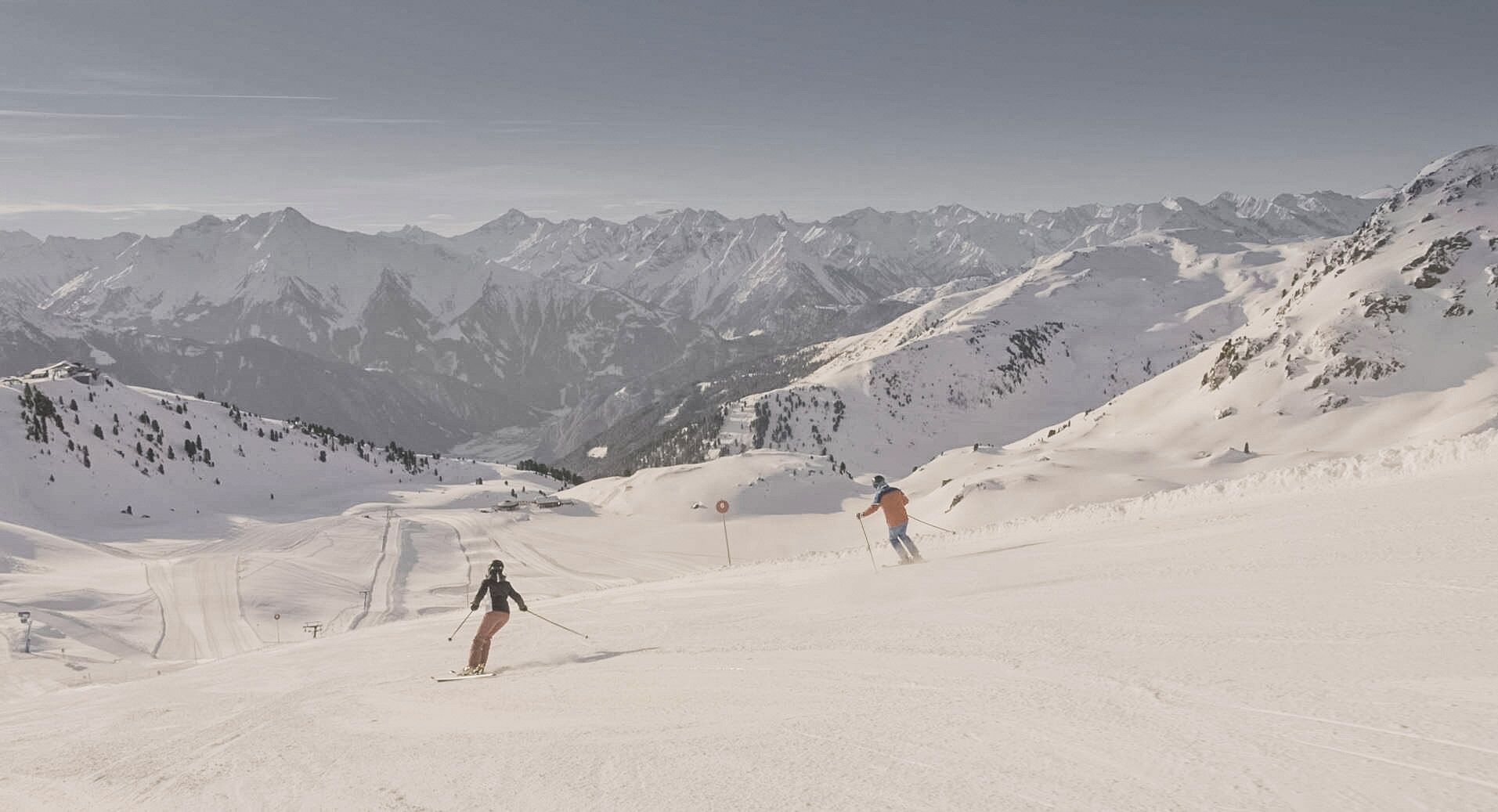 A snowy mountain slope with skiers and a clear view of distant mountains.