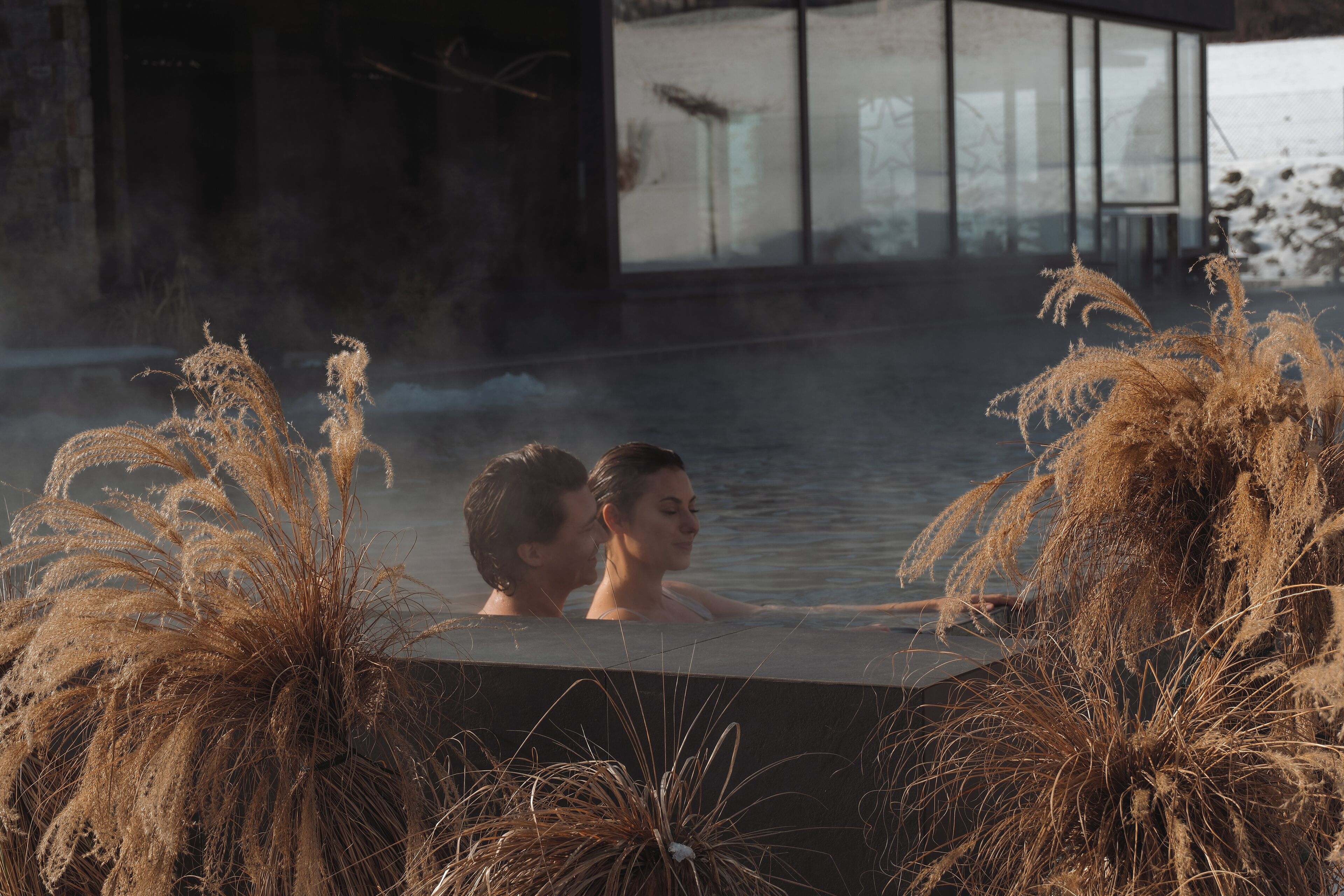 Una pareja en un jacuzzi rodeado de altas plantas de pasto seco.
