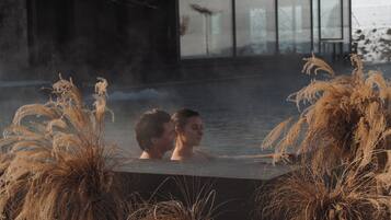 Una pareja en un jacuzzi rodeado de altas plantas de pasto seco.