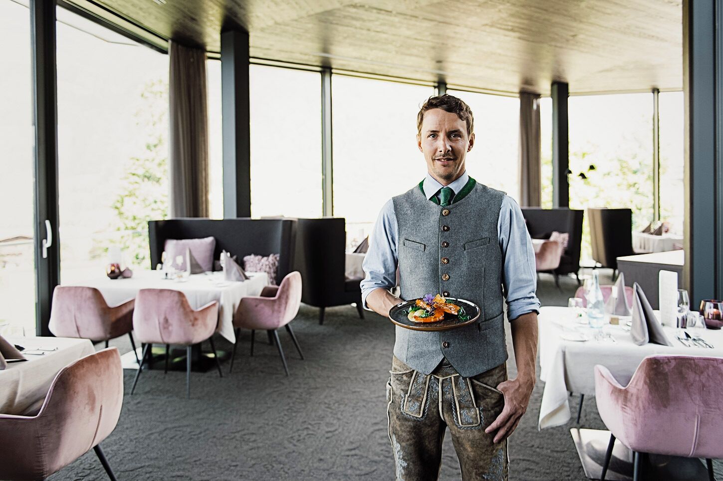 A person holding a plate of food in a modern restaurant with tables and chairs.
