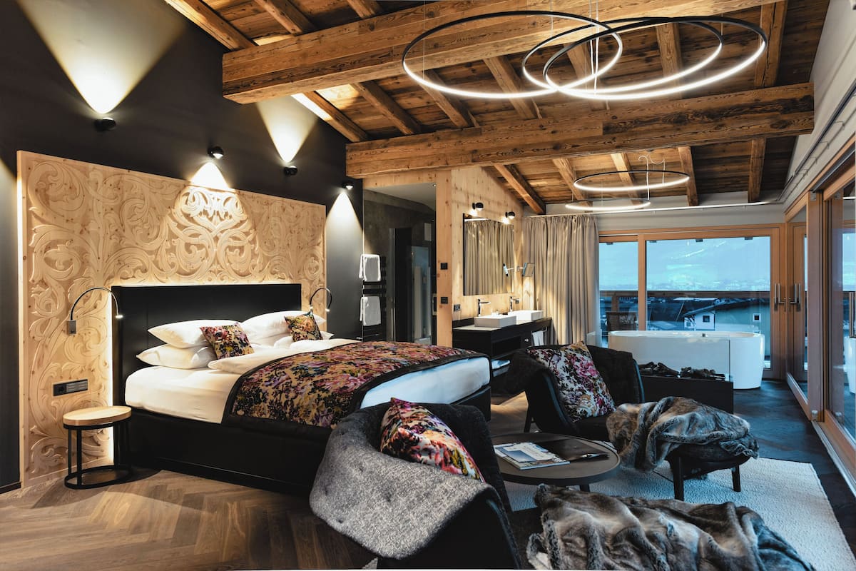 A modern bedroom with a large bed, a sitting area, and a view of the city.