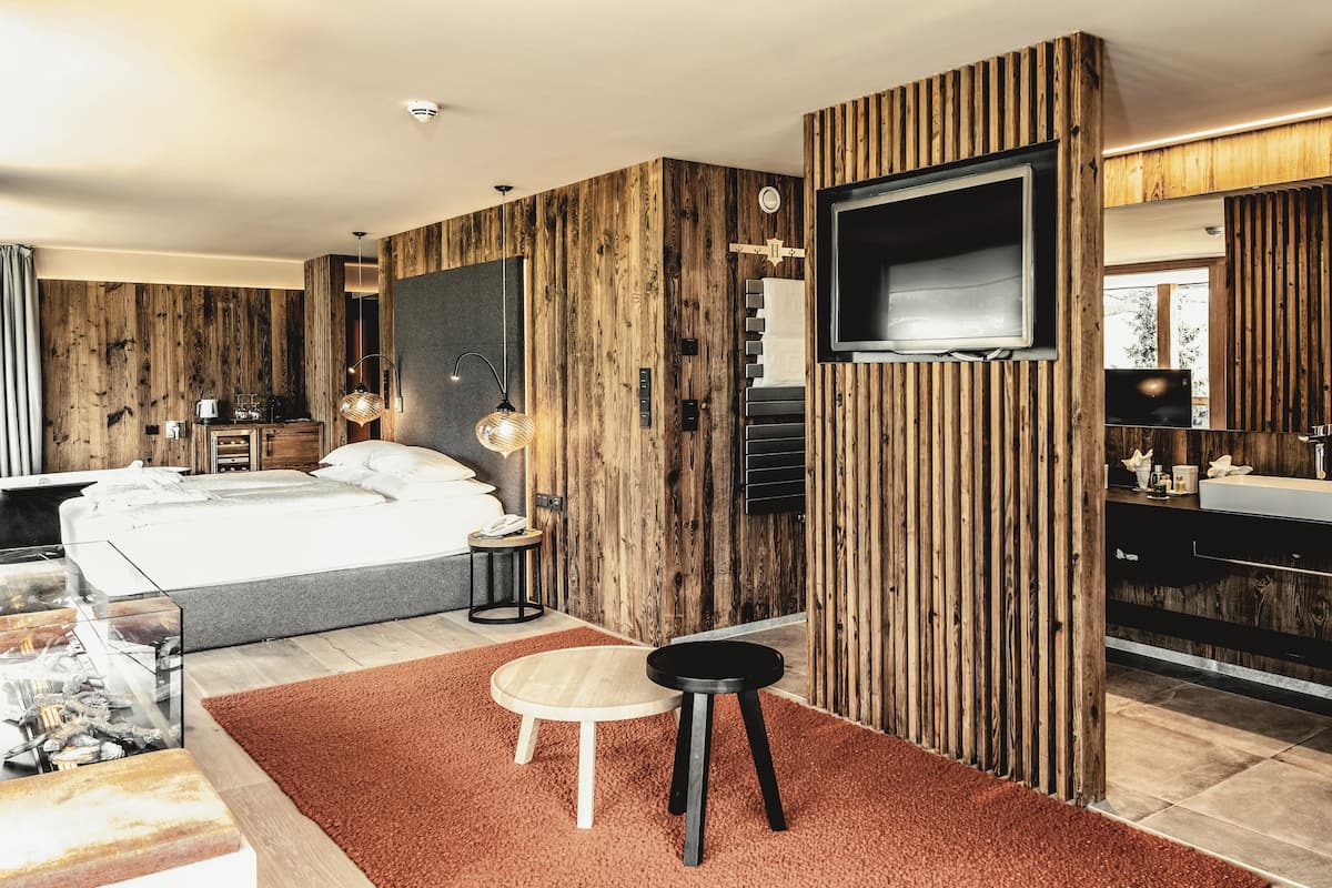 A modern bedroom with a large bed, wooden panel walls, a TV, and a bathroom with a mirror and sink.