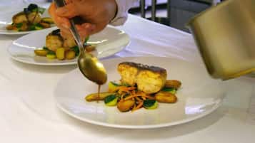 A chef pouring sauce onto a plated dish.