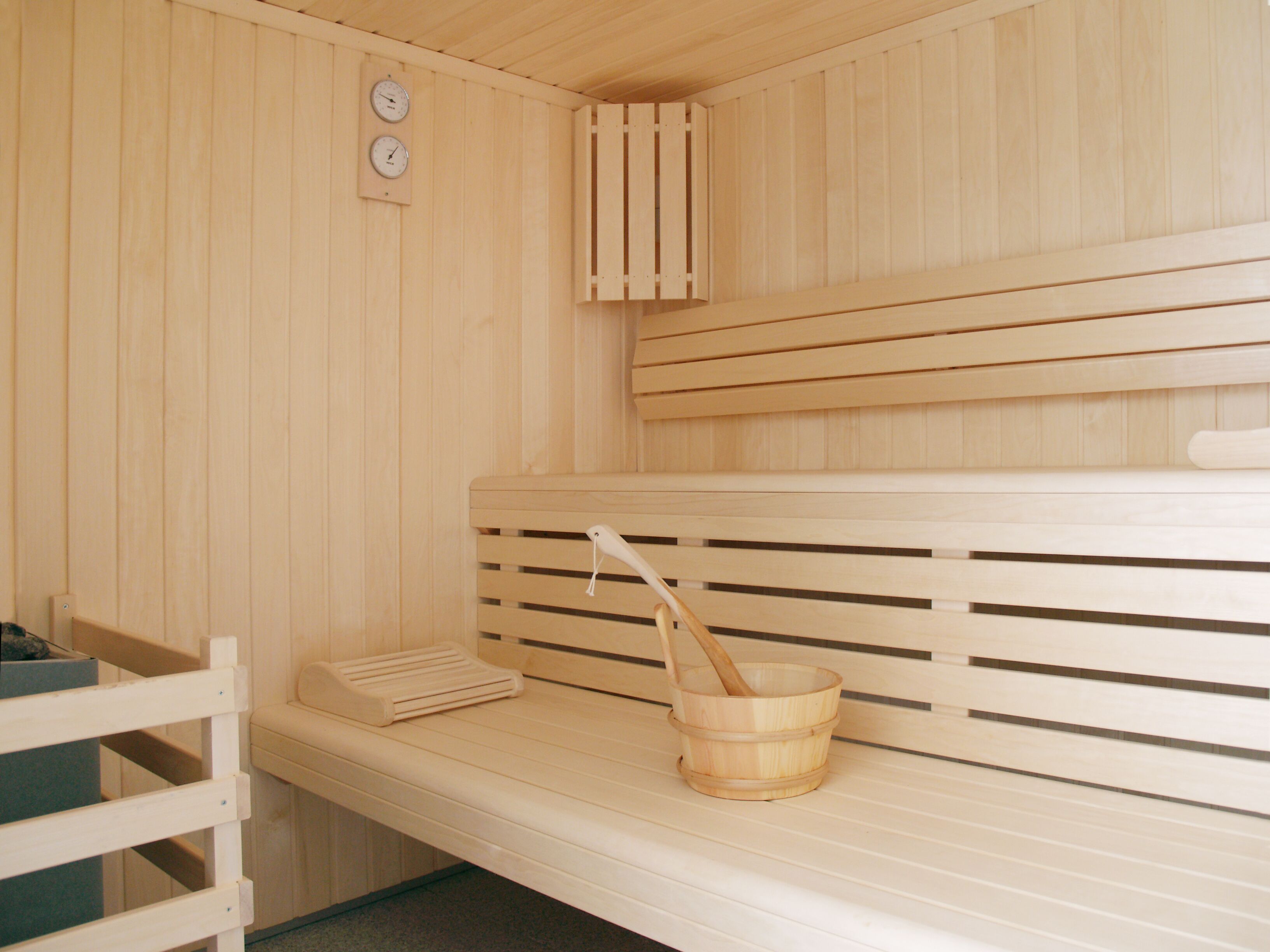 A sauna with wooden benches, a wooden bucket, and two wall-mounted clocks.