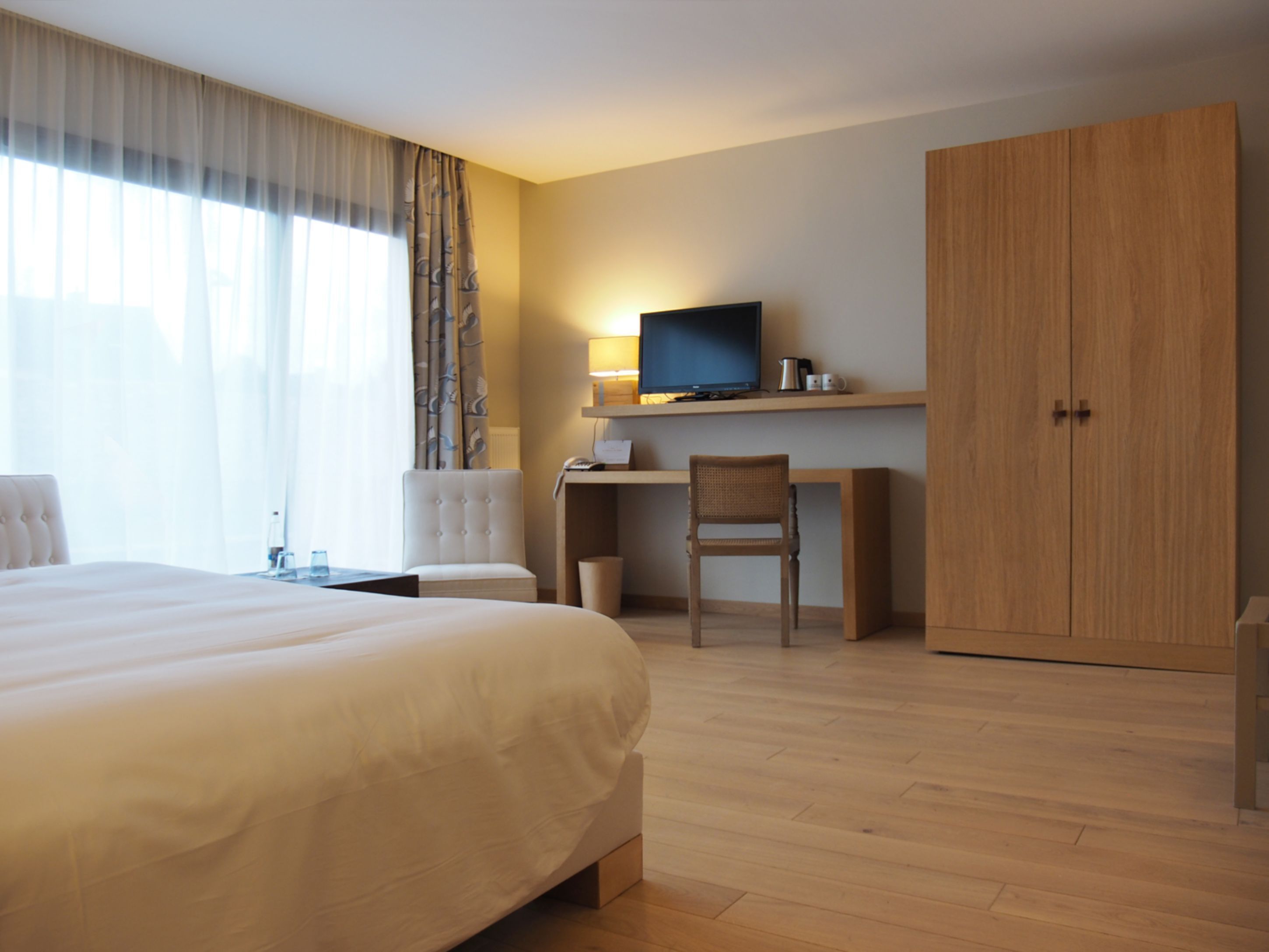 A hotel room with a large bed, a desk with a computer, a chair, and a wardrobe.