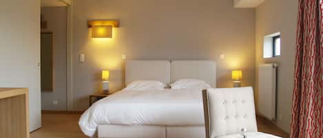 A hotel room with a large bed, two bedside tables with lamps, a wooden nightstand, a small table with glasses and a bottle, and a red patterned curtain.