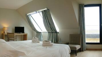 A hotel room with a bed, a desk, a chair, a TV, and a window with curtains.