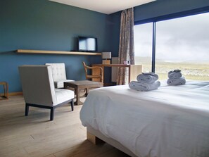 Habitación de hotel con cama, escritorio, silla, televisión y vistas a la playa.