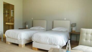 Habitación de hotel con dos camas, piso de madera, una silla y una mesa con una botella y vasos.