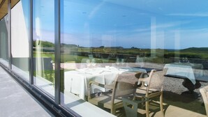 Un espacio moderno para comer al aire libre con paredes de vidrio, vistas despejadas del paisaje y una mesa lista para dos.