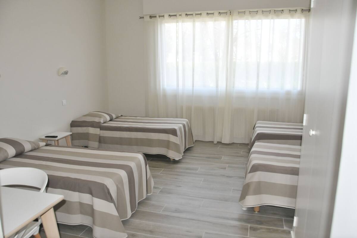 Camera d'albergo con due letti singoli, un tavolino e una sedia.