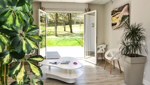 A modern room with a glass door leading to a garden, a white table, and a potted plant. - Domaine du Pignada (Anglet)