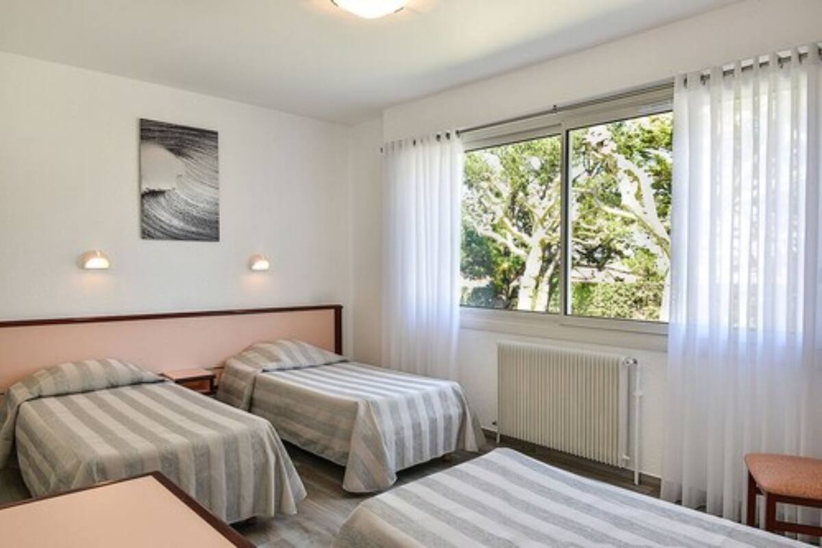 Una camera d'albergo con due letti singoli, una finestra con tende, un termosifone e un'opera d'arte appesa al muro.