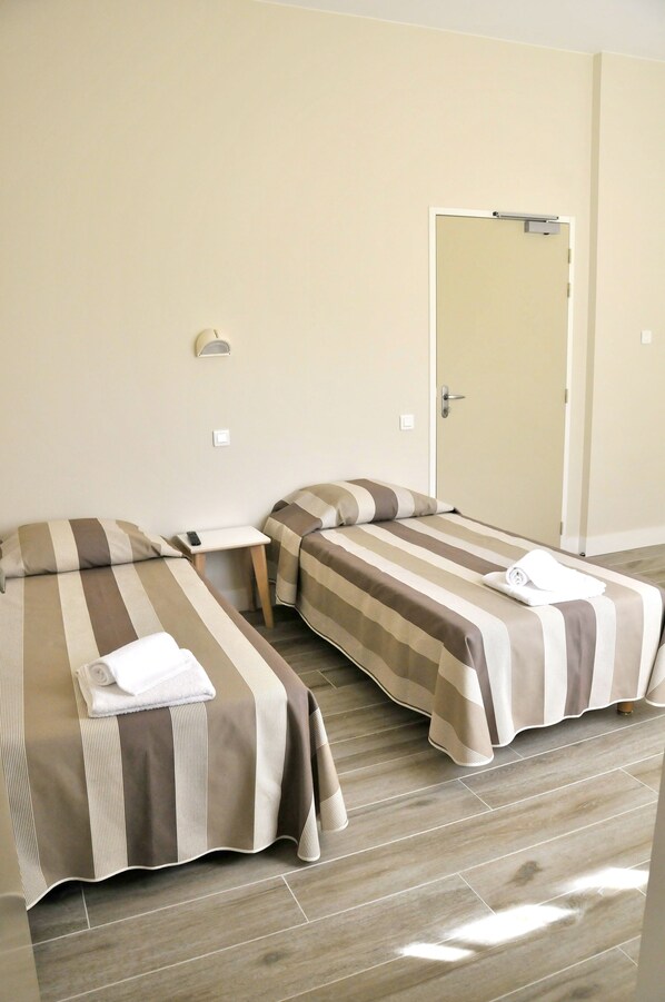 A hotel room with two beds, a small table, and a door.