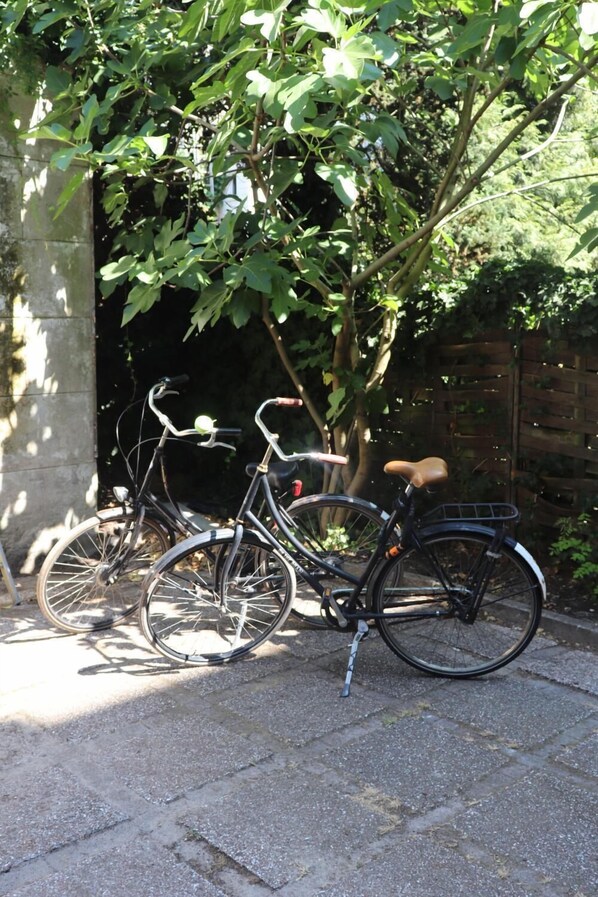 A bicycle parked in a shaded area with a tree and a brick wall in the background.