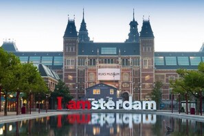 A historic building with a prominent sign for the Rijks Museum, surrounded by a reflective water feature and trees.