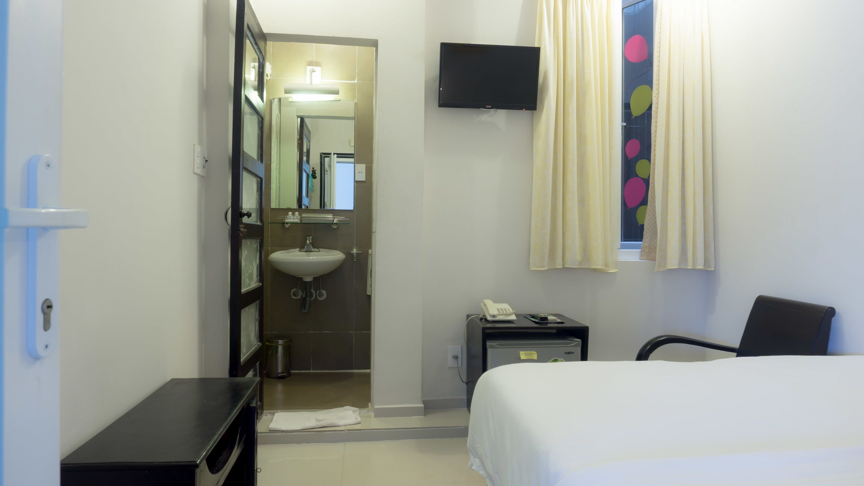 A hotel room with a bed, a desk, a telephone, a mirror, a sink, and a television.
