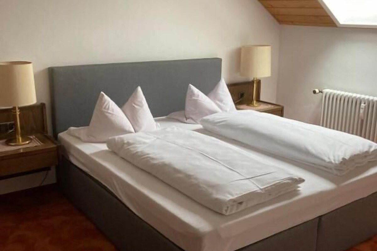 A neatly made bed with white linens and pillows, a grey headboard, and two bedside lamps on wooden nightstands.