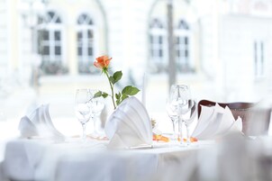 Una mesa dispuesta para comer, con una rosa y copas, en una habitación con ventanales abovedados.
