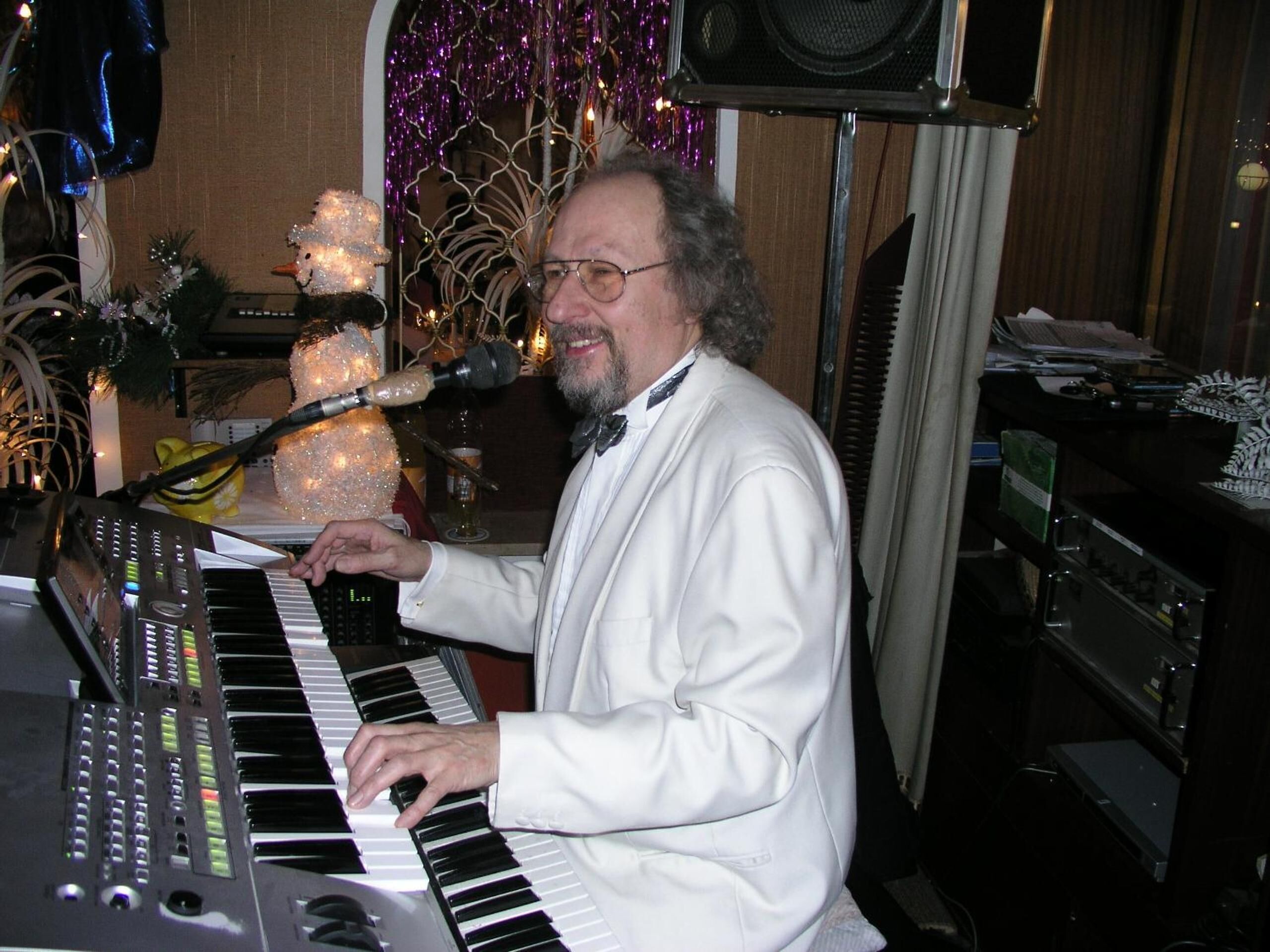 A person playing a keyboard in a room with a decorative Christmas tree and various items on shelves.