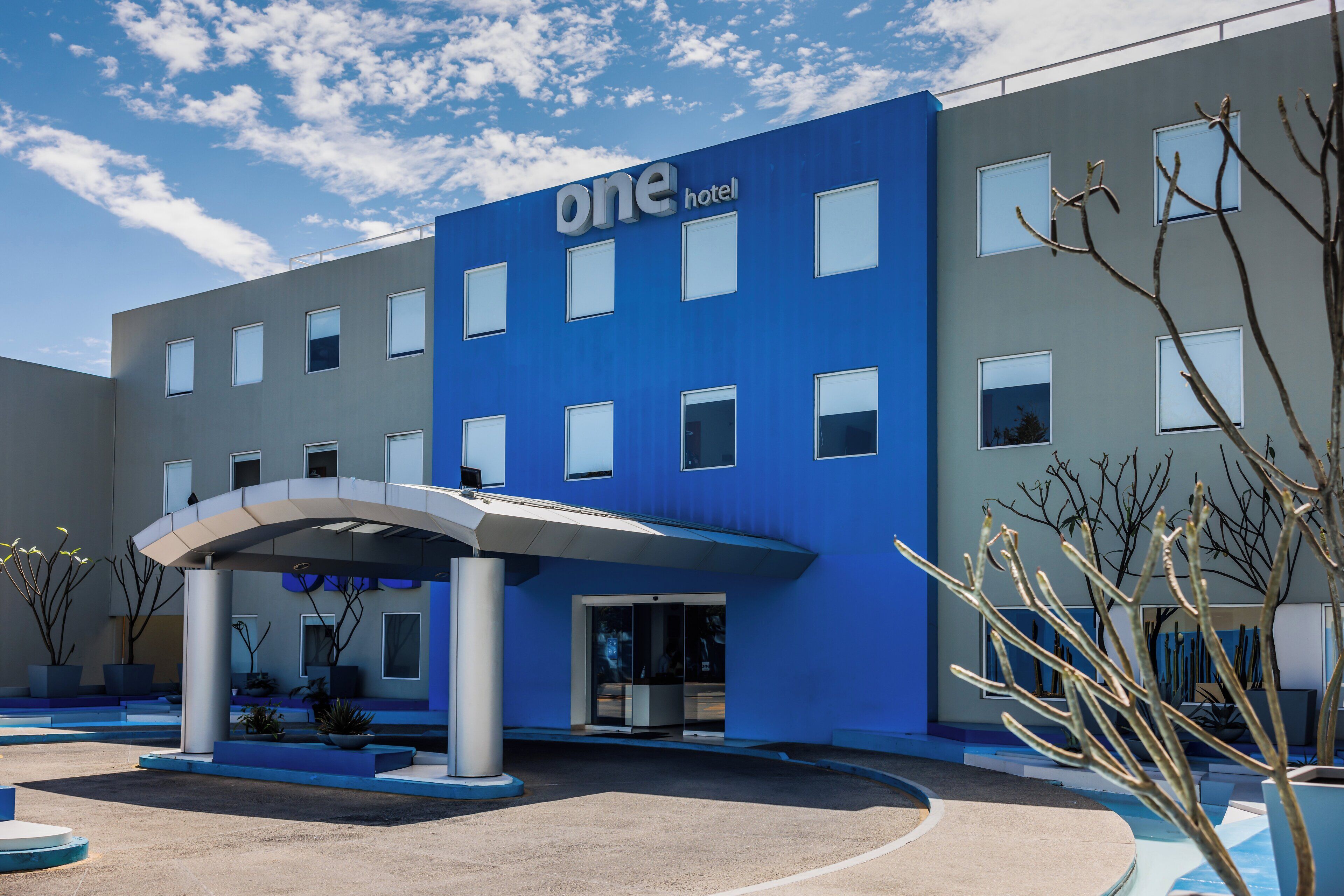 A modern hotel with a blue facade, multiple windows, and a covered entrance area.