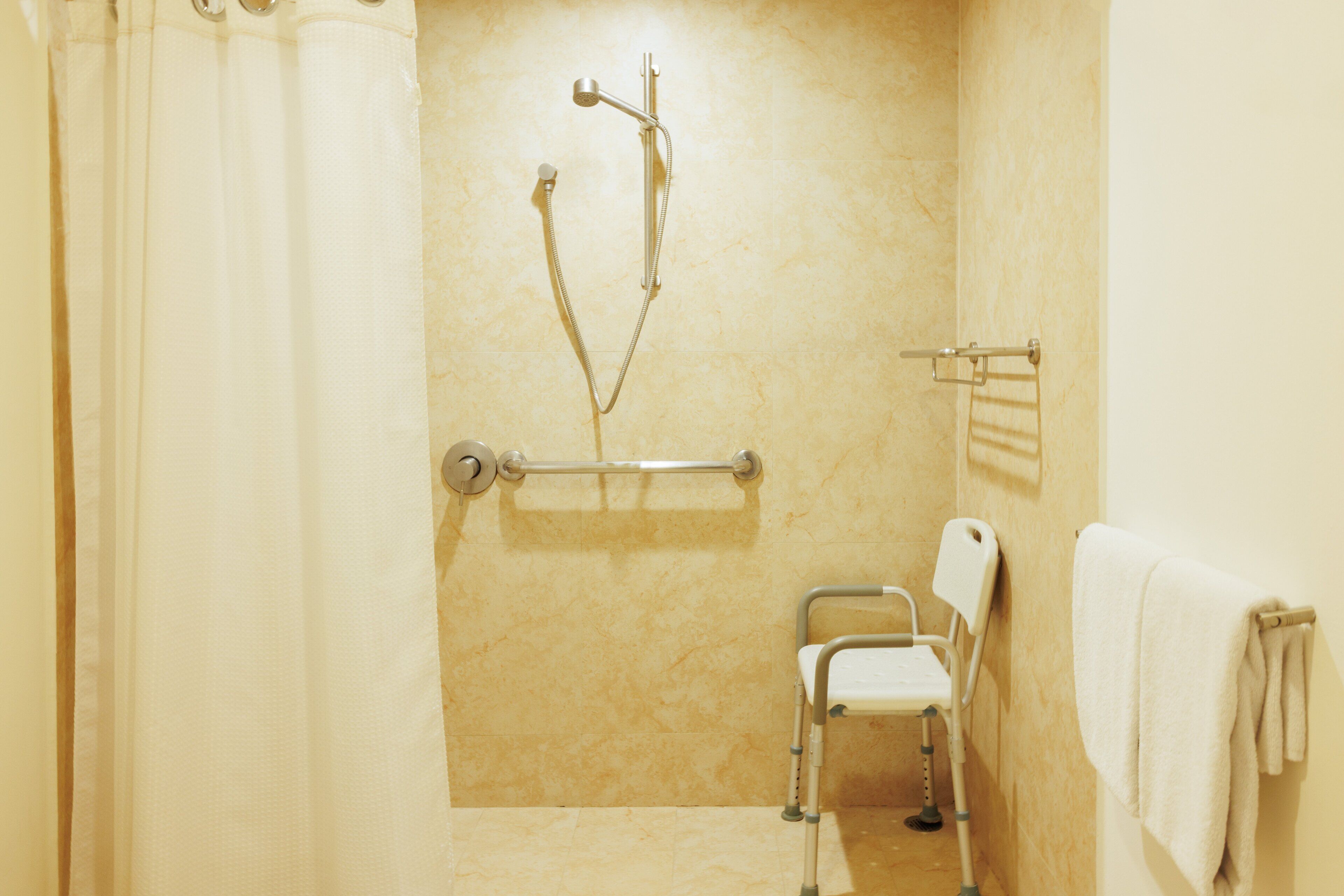 A bathroom with a shower, a grab bar, a wheelchair-accessible chair, and a towel rack.