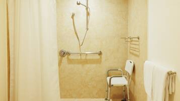 Baño con ducha, barra de apoyo, silla accesible para sillas de ruedas y toallero.