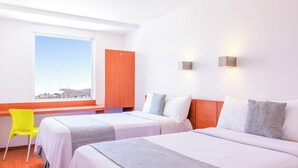 Habitación de hotel con dos camas, una ventana con vistas, una puerta de madera y una silla de color amarillo brillante.