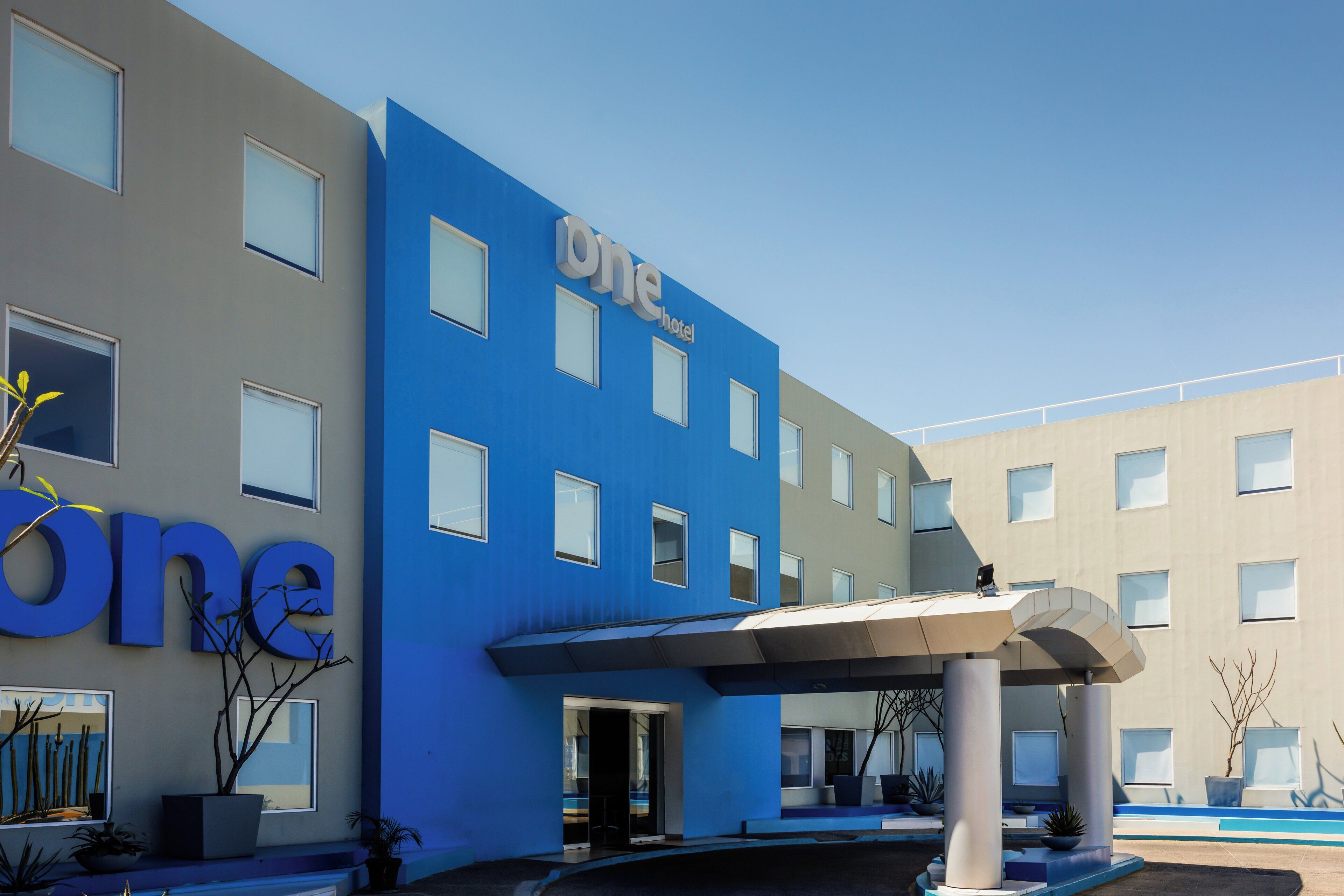 A modern hotel with a blue facade, a covered entrance, and a clear sky.
