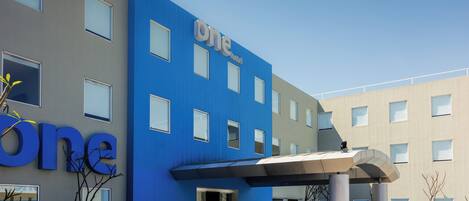 A modern hotel with a blue facade, a covered entrance, and a clear sky.