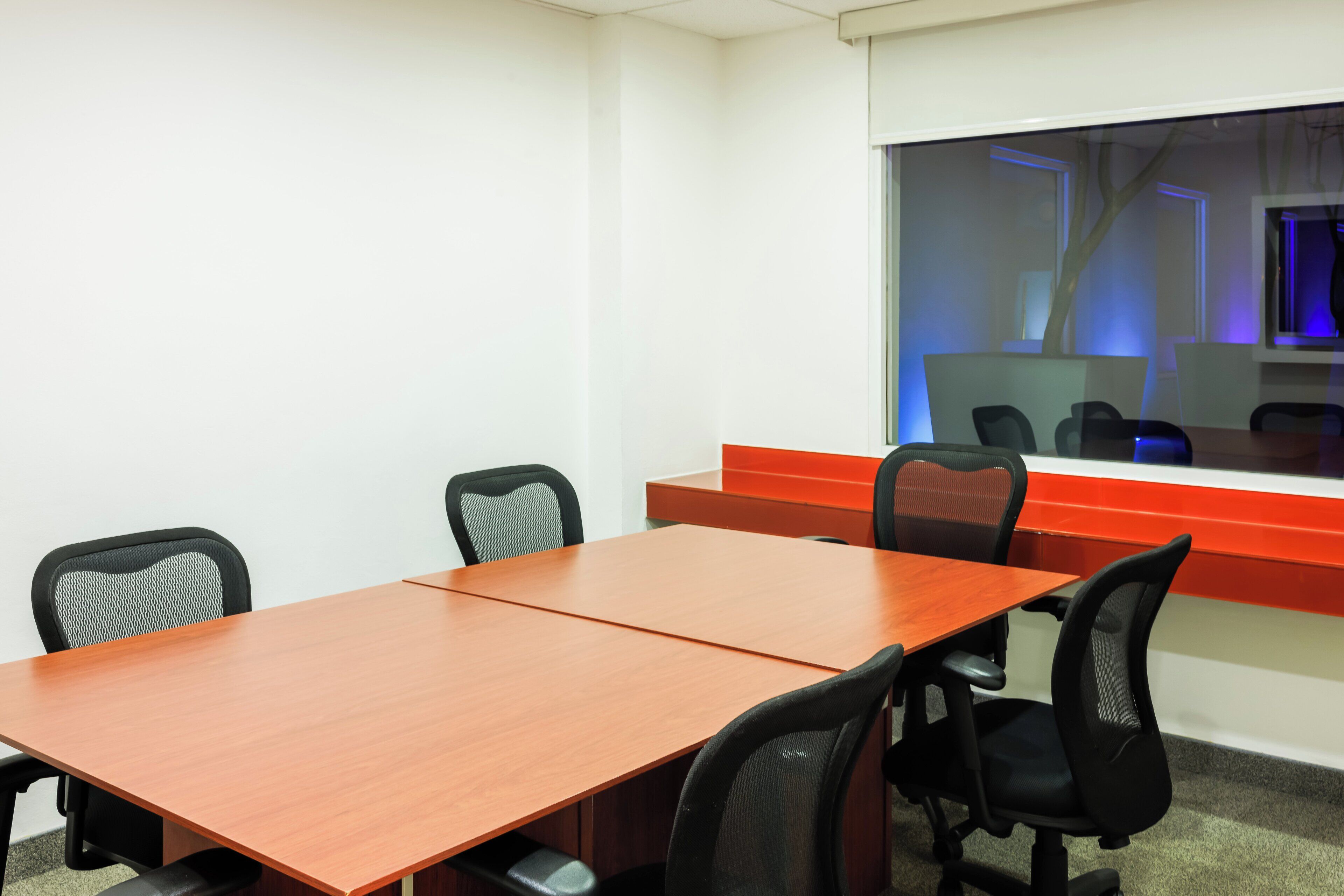 Una sala conferenze con tavolo in legno, sedie da ufficio nere e una parete rossa a contrasto.