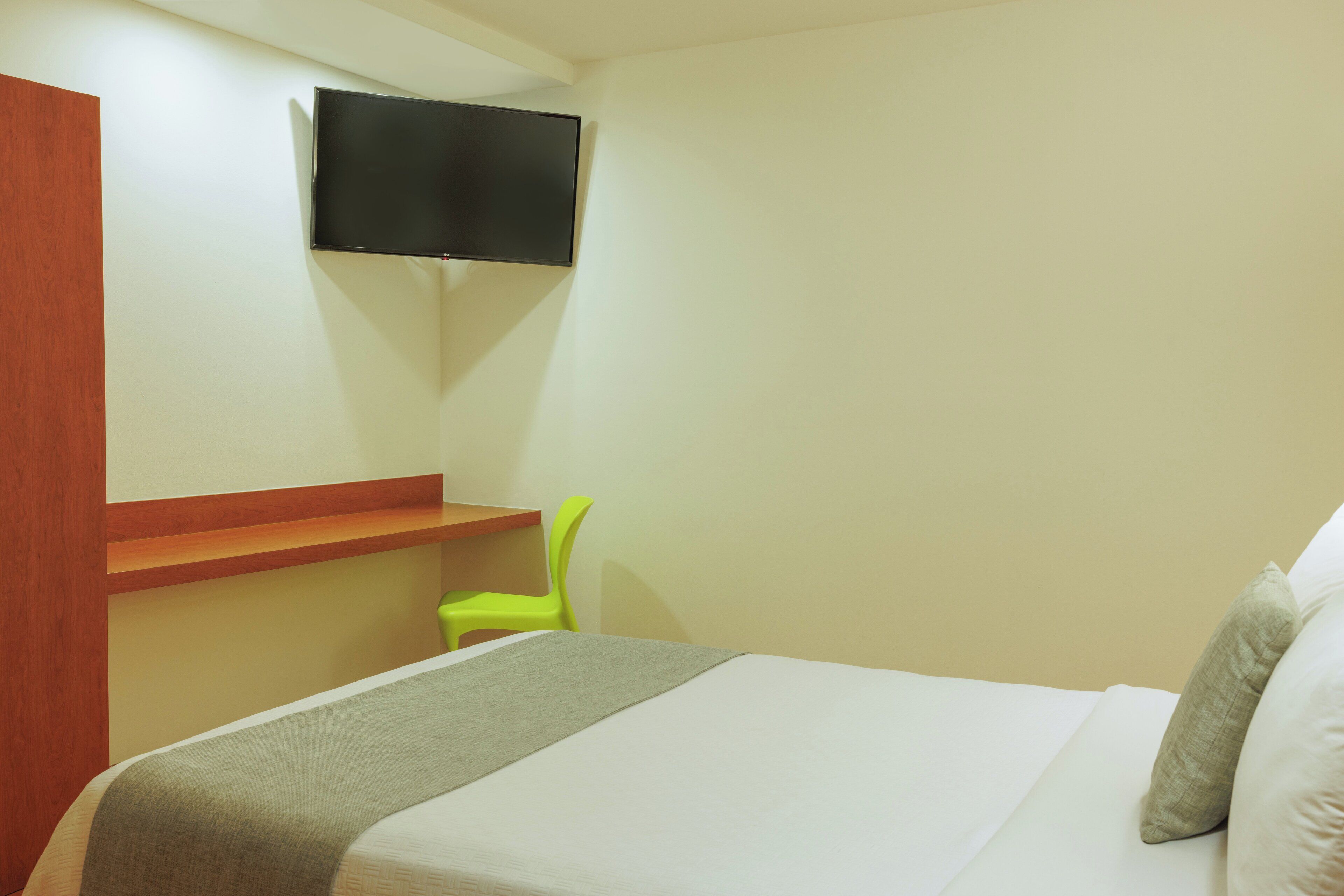 Ein Hotelzimmer mit einem Bett, einem an der Wand befestigten Fernseher, einem kleinen Tisch und einem grünen Stuhl.